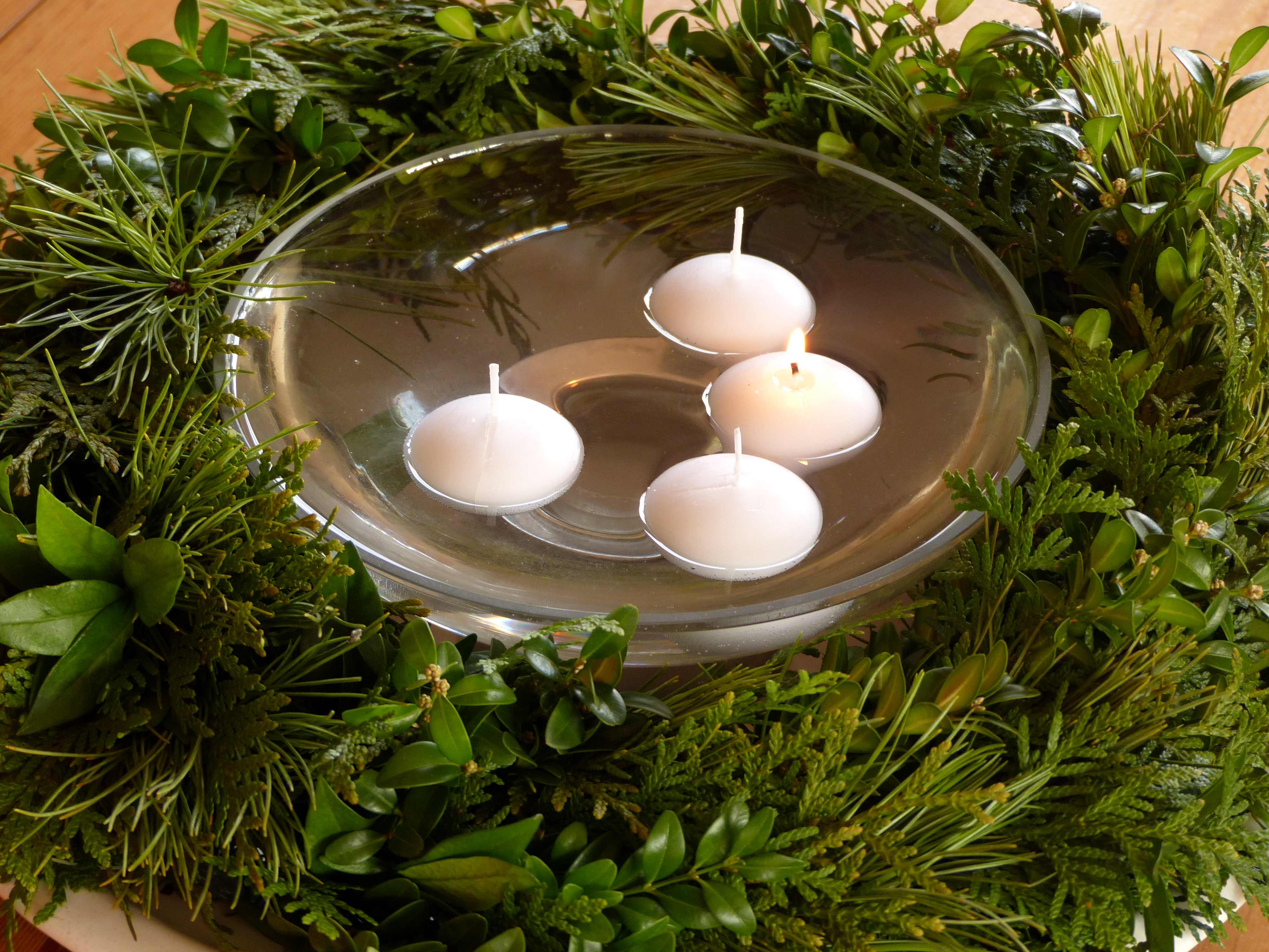 <p>Dieser Adventkranz liegt auf einem großen, weißen Teller. Er wurde um eine Glasschüssel, in der 4 Kerzen schwimmen, gelegt. Sein Kern besteht aus einem Weidenreifen. So kann er, um sich zu erfrischen, von Zeit zu Zeit in eine Schüssel voll Wasser gelegt werden.</p>