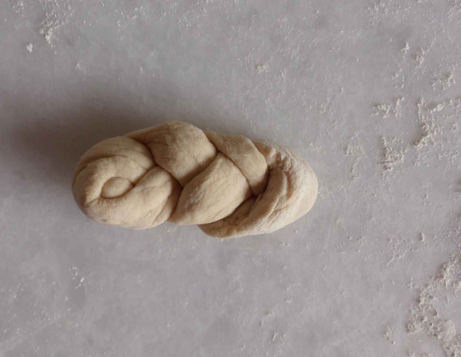 <p>Einstrangzopf - 6. Schritt:<strong> </strong></p><p>Das freie Teigende wurde von oben durch die verbliebene kleine Schlaufe gefädelt.</p>