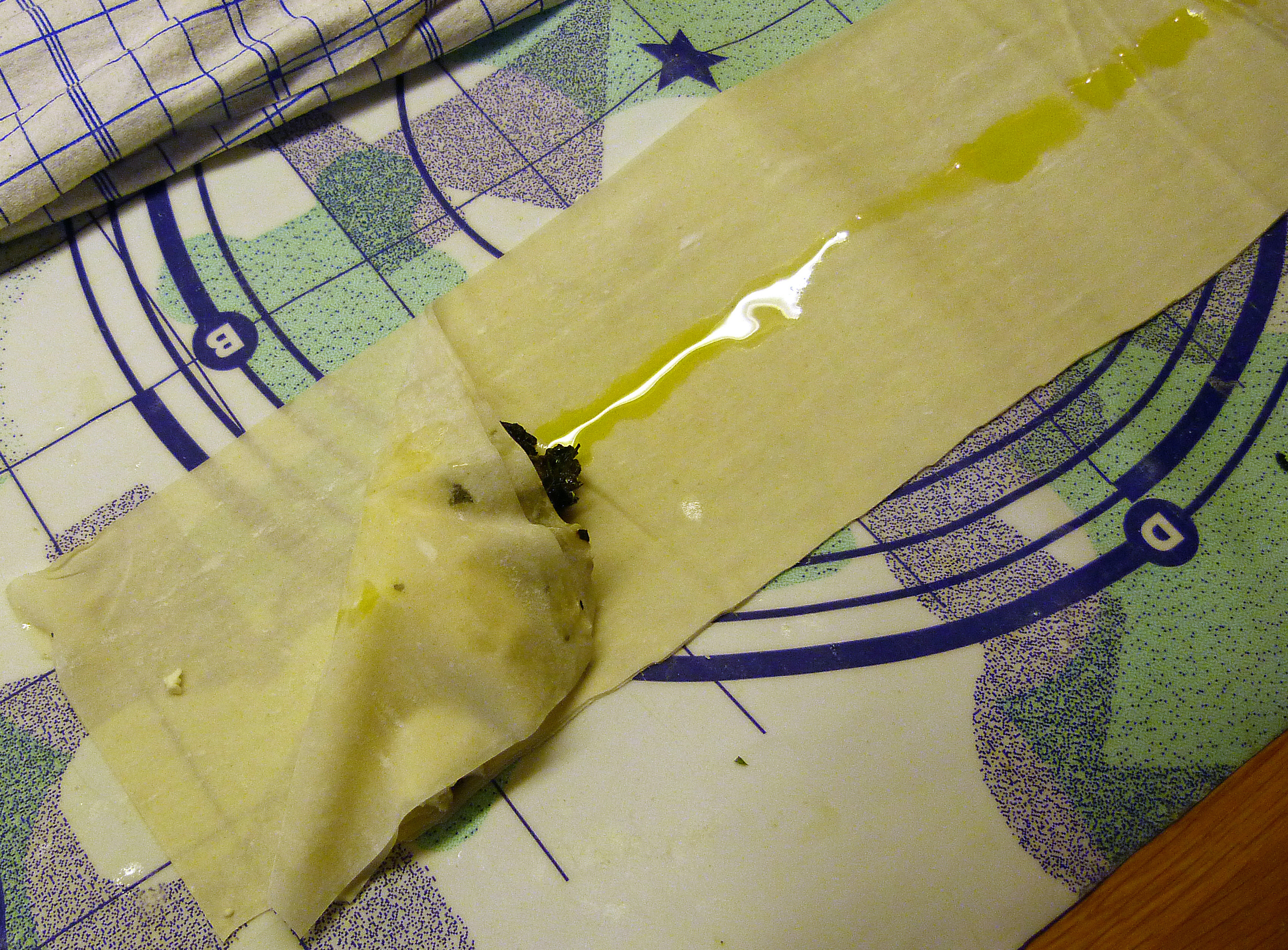 <p>Die linke obere Ecke über die Fülle zum unteren Teigblattrand hin falten. Dazu nimmt man, siehe Foto, zwei der Teigstreifen.</p>