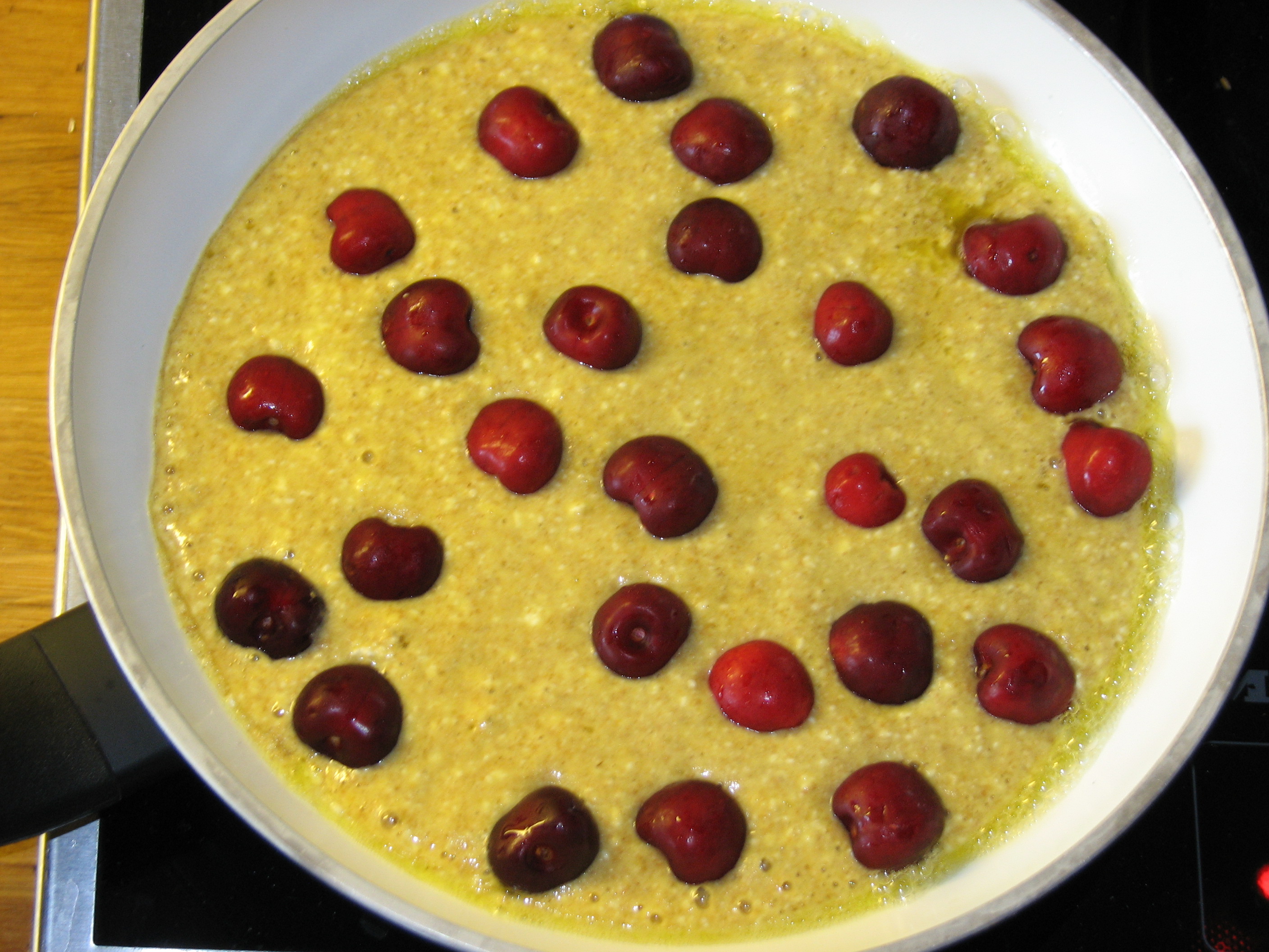 <p>Sauerrahmteig in der Pfanne mit Kirschen bestreut.</p>