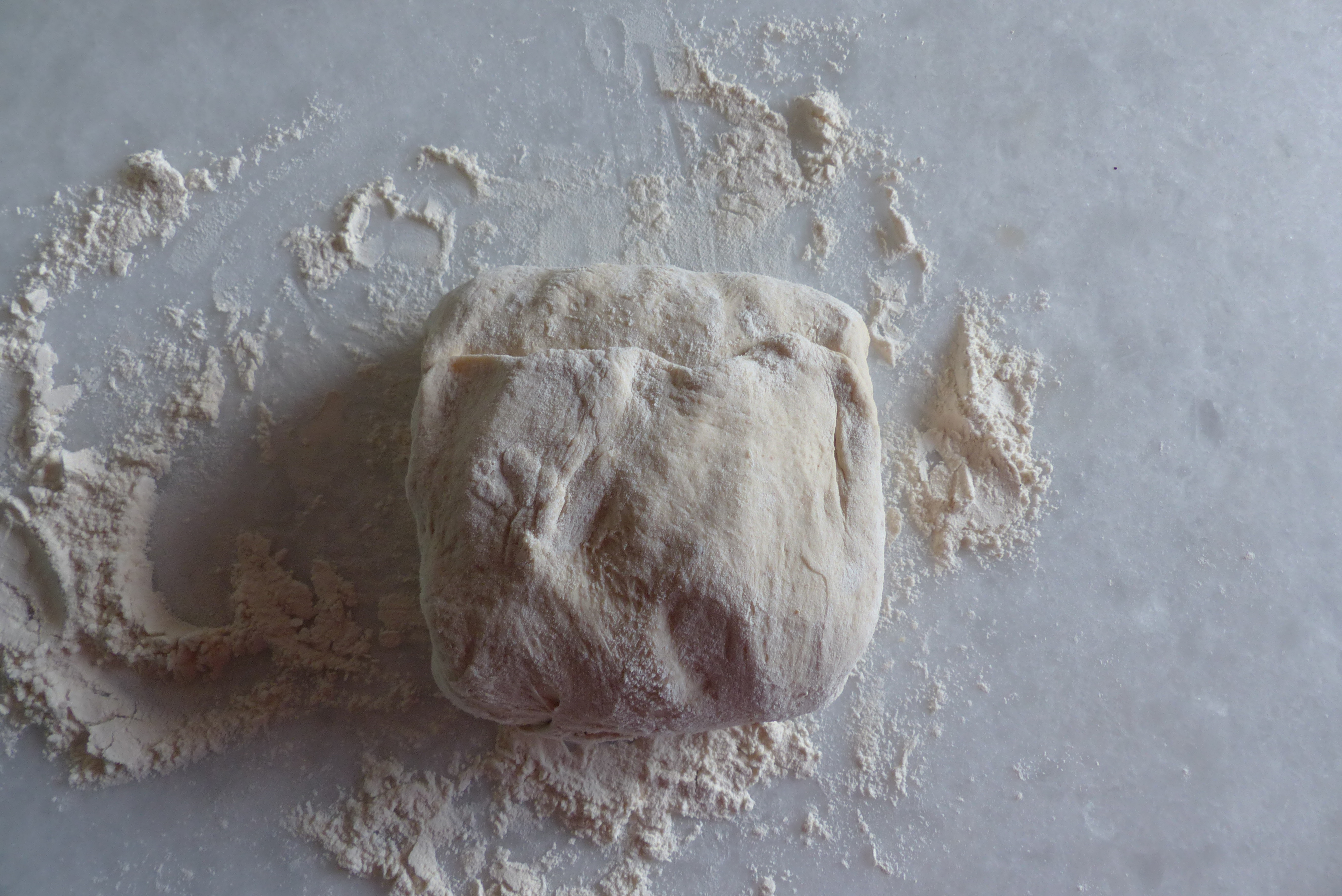 <p>Die schmalen Seiten wieder übereinander legen, sodass ein q<em>uadratisches Teigpaket entsteht.</em></p>